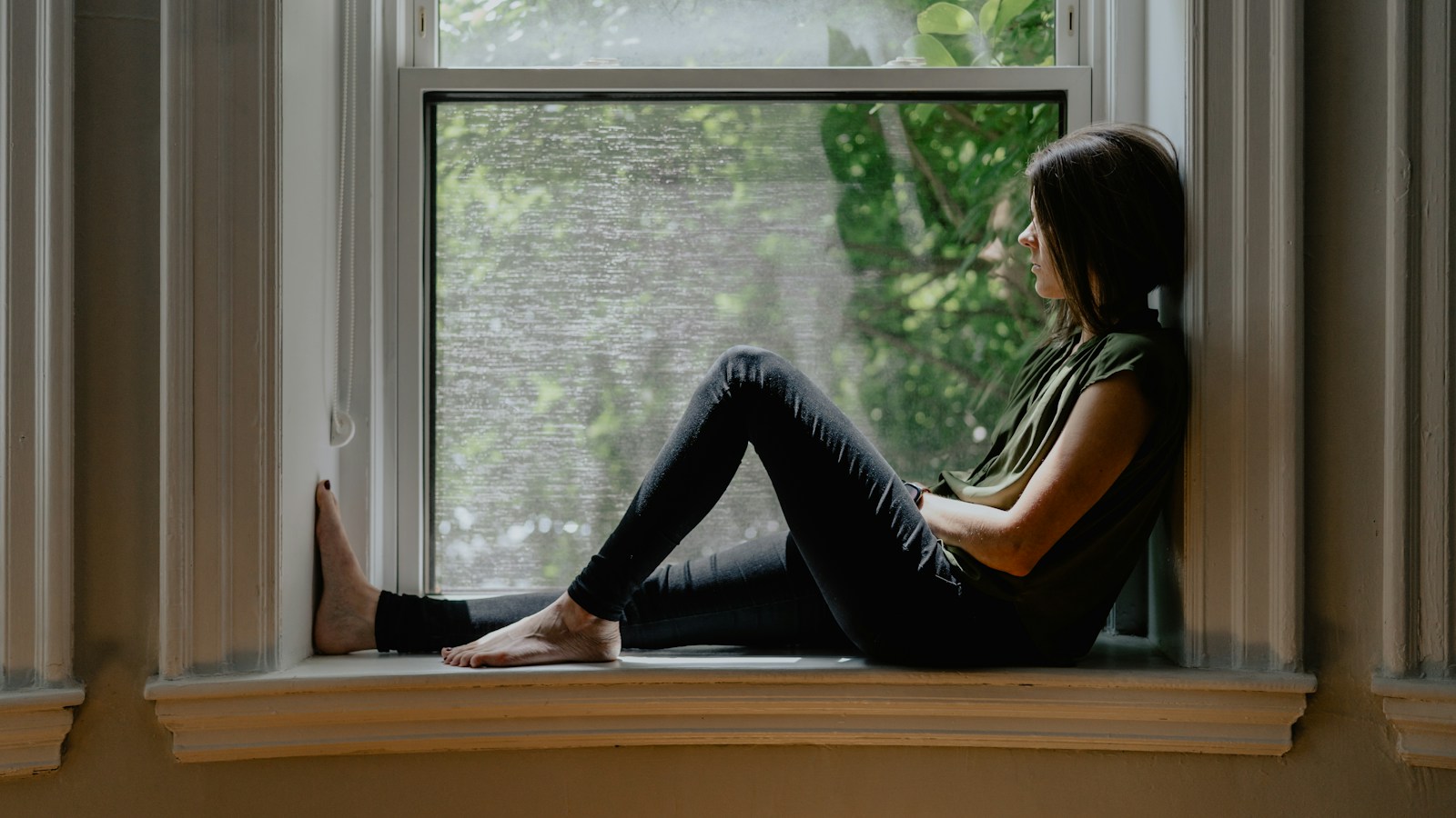 Person sitting quietly by a window while reflecting after a relationship betrayal